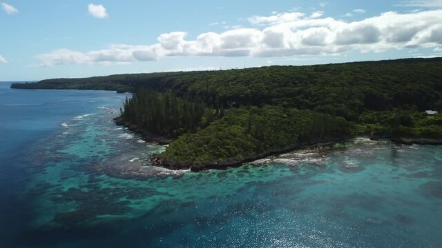 Aerial circling above rugged coastline and emerald crystal waters on Maré Island, New Caledonia