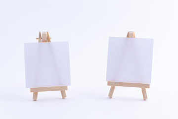 Two Wooden Easels Miniature with Blank White Square Canvas for Artists and Painters - Mockup. Mini Wooden Stand with Clean Artboard on White Background, Copy Space