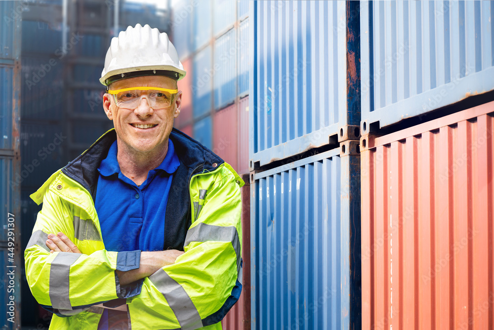 Wall mural Factory engineer worker man standing confidence with green working suite dress and safety helmet n front of container and cargo space. Business people working in shipping transport industry.