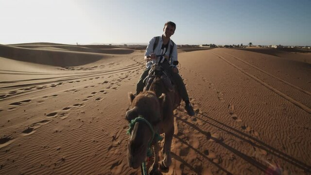 Backwards tracking of following camel rider. Tourists riding on tamed animals in desert. Morocco, Africa