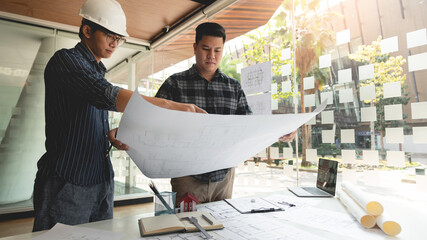 two male colleagues collaborating an architecture project about rooms’ position in a blueprint