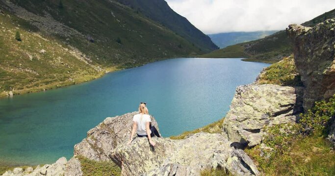 Young woman enjoying the mountain lake view in the austrian alps with amazing colerfull landscape. Blue mountain lake with fresh water young girl sitting and relaxing in awesome alpine scenery. 4K