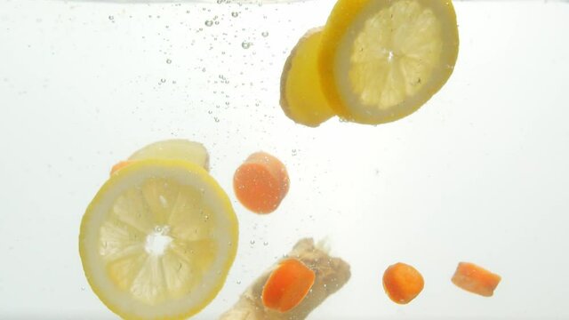 Freshly chopped lemon and carrot dropped into water, isolated white background