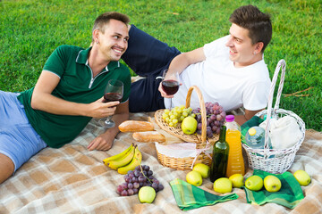 Two happy european males friends gaily spending time together on picnic drinking wine.