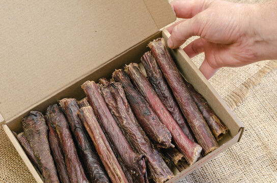 Hand holds cardboard box of dog treats. Sticks of dried beef eso