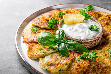 Zucchini pancakes with herbs and sour cream on a plate close-up. Vegetarian dish