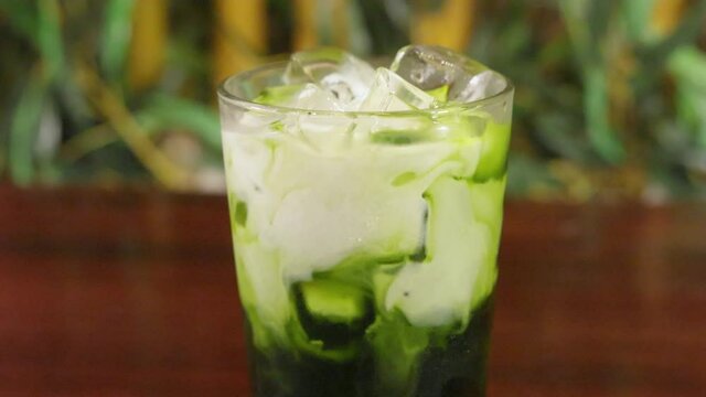 Cream slowly poured into refreshing matcha green tea drink, slider close up slow motion 4K