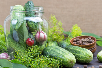 Garlic, cucumbers and cherries in glass jar. Cucumbers and dill on table