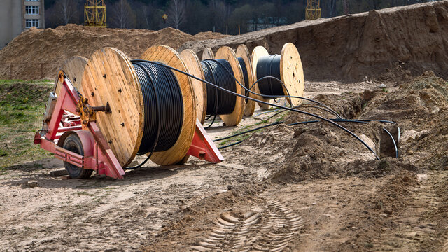 Cable high voltage electric in roll or round coil on ground. Concept of electricity supply for construction projects. Several wooden coils with power cable laid in trench 16x9 image.