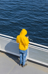 A young boy with a smartphone in his hands standing on the deck of the ferry traveling on the ocean.