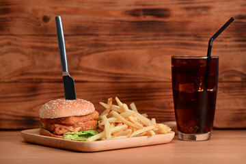 Delicious fish burger with fried potatoes and soft drink on wooden table.