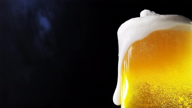 Beer is pouring into a beer mug with bubbles close-up on a black background. Overflowing beer glass with flowing foam. 4k slow motion video.