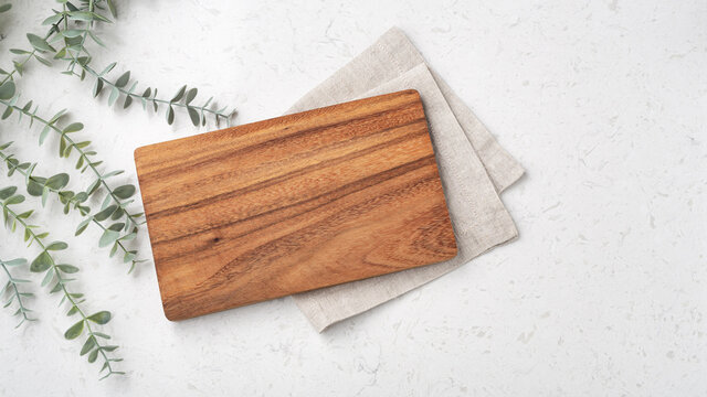 Wood cutting board with linen napkin and plant on marble table