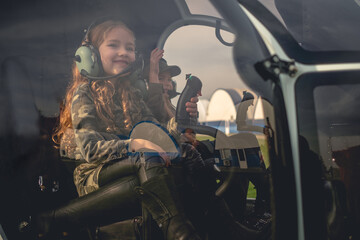 Smiling preteen girl in pilot headset with friend in helicopter cockpit