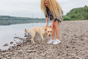 Young woman playing with her labrador retriever dog on the river shore