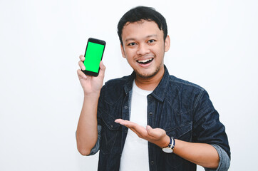 Young Asian man is standing and smiling pointing on green screen on smartphone screen on white background.