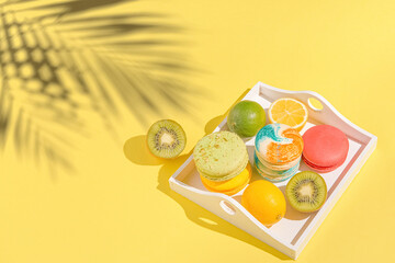 Colorful macaroons with lemon, lime  and kiwi on white tray on sulit yellow background with shadows...