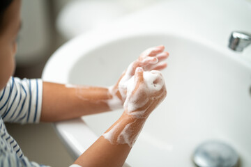 Small child washing her hands with soap in the sink.