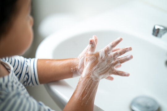 Small child washing her hands with soap in the sink.