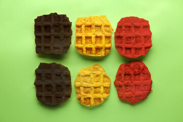Delicious waffles in colors of Belgian flag on green background