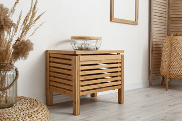 Wooden chest of drawers with basket near light wall