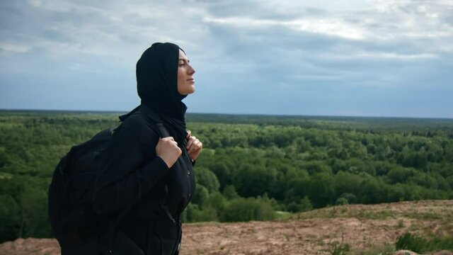 Muslim woman with backpack contemplating natural scenery from mountain top enjoying freedom