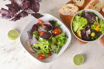 Bowls with tasty fresh salad, bread and lime on light background