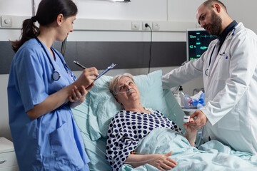 Doctor checking senior patient in hospital intensive care, checking oxygen saturation, blood...