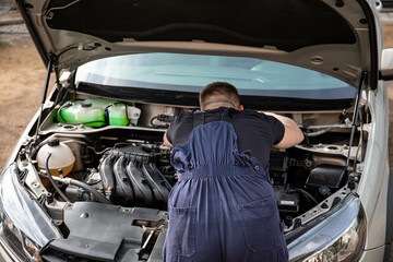 a man repairs a car. a man in blue special clothes to repair the car. engine parts machine repair...