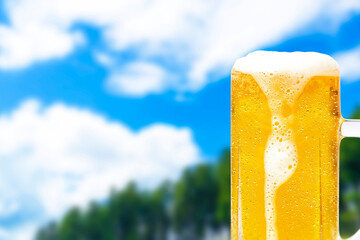 Image of a fresh green background and a mug of beer with dripping foam and drops of water.