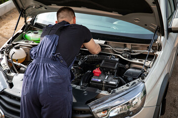 a man repairs a car. a man in blue special clothes to repair the car. engine parts machine repair maintenance breakage problem hands people man master