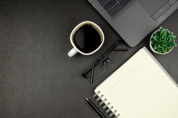 Modern working space. Laptop, coffee cup, glasses, blank notepad with pen and home plant on black desk