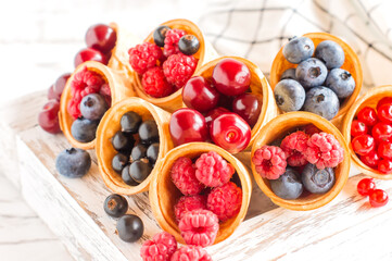 juicy berries in waffle crispy cones in a white wooden box on a white background. front view.