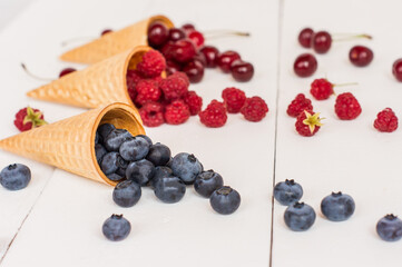 appetizing waffle cones with blueberries, raspberries, cherries on a white wooden background. Summer dessert