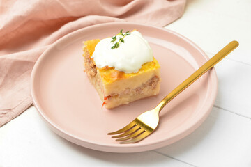 Plate with piece of mashed potato casserole and sour cream on light wooden background, closeup