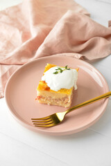 Plate with piece of mashed potato casserole and sour cream on light wooden background