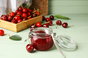 Glass jar with sweet cherry jam on color wooden background