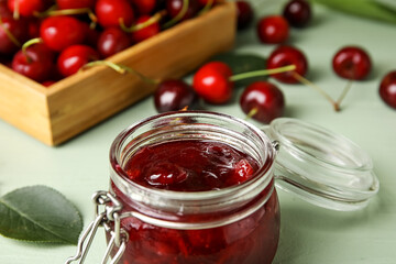 Glass jar with sweet cherry jam on color wooden background, closeup