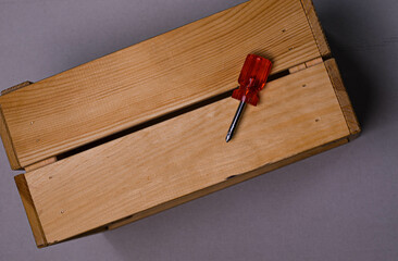 brown wooden box on a white background with a red phillips screwdriver background texture.the screwdriver is lying on a wooden box. the twisted screw is handmade. the box is handmade. wooden box with
