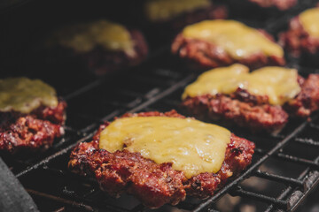 Burgers on the grill with gorm cheese melting on top of the meat. Meat cooked on the grill and charcoal. Heat on meat for cooking. Grilled meat for burger. Pork sandwiches. Cooking pork. Food.