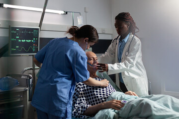 African doctor helping senior patient breath using repiratory ventilation tube, in hospital room intensive care. Old man hospitalized checked by medical staff and getting treatment.