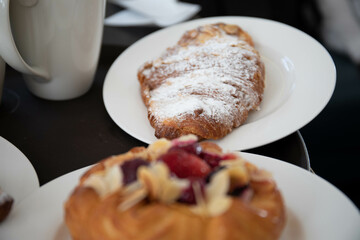 an almond croissant and a bun with strawberry slices lie on a white plate next to a white cup of coffee cappuccino and latte food fresh pastries bakery handmade kitchen cafe breakfast health