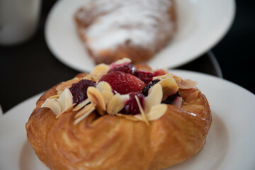 an almond croissant and a bun with strawberry slices lie on a white plate next to a white cup of coffee cappuccino and latte food fresh pastries bakery handmade kitchen cafe breakfast health