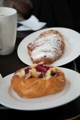 an almond croissant and a bun with strawberry slices lie on a white plate next to a white cup of coffee cappuccino and latte food fresh pastries bakery handmade kitchen cafe breakfast health