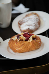 an almond croissant and a bun with strawberry slices lie on a white plate next to a white cup of coffee cappuccino and latte food fresh pastries bakery handmade kitchen cafe breakfast health