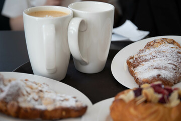 an almond croissant and a bun with strawberry slices lie on a white plate next to a white cup of coffee cappuccino and latte food fresh pastries bakery handmade kitchen cafe breakfast health