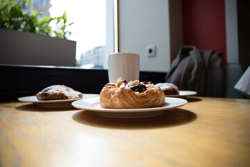 an almond croissant and a bun with strawberry slices lie on a white plate next to a white cup of coffee cappuccino and latte food fresh pastries bakery handmade kitchen cafe breakfast health