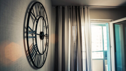 Big round black classical clock hangs on wall of kitchen room