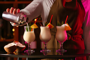Female bartender making tasty Pina Colada cocktail on table in bar - obrazy, fototapety, plakaty