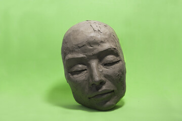 Female face in clay on green background. Sculpture with Caucasian features, closed eyes, calm expression: in process of creation.